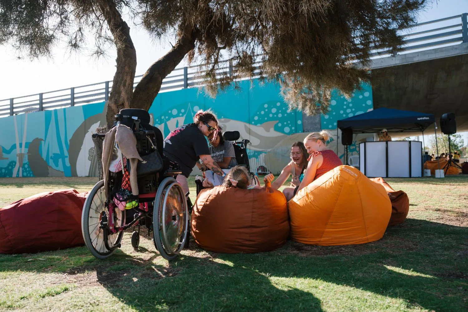 Young people with disability and support workers sitting together on beanbags in a relaxed outdoor space.